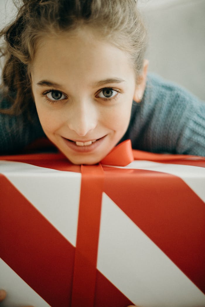 services-04 A cheerful girl smiling warmly while hugging a large red and white gift box indoors.