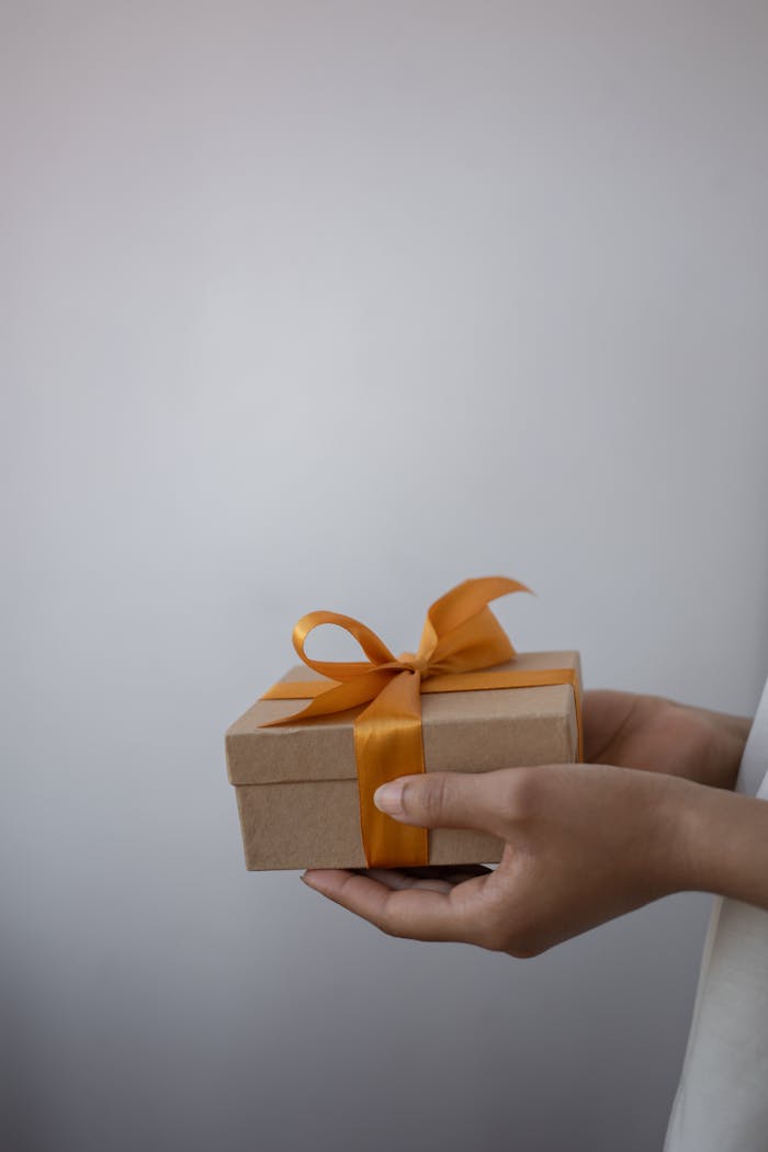 about-01 A close-up of hands holding a gift box decorated with an orange ribbon bow.