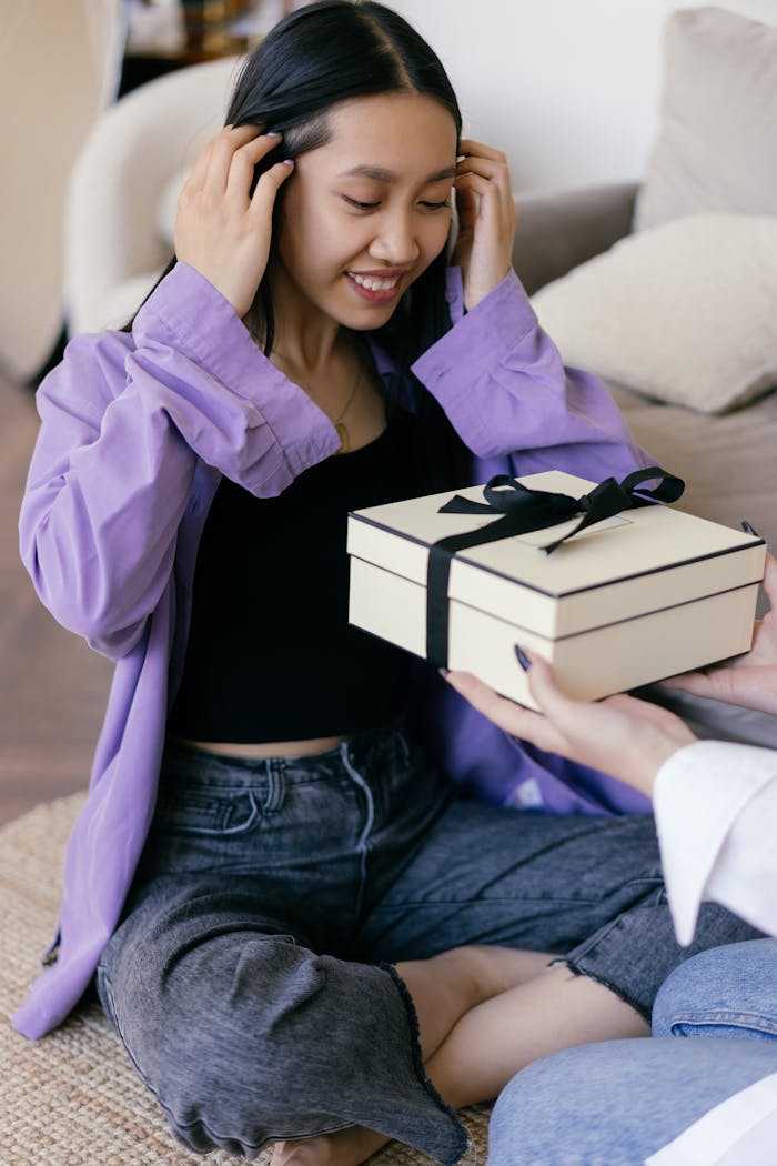 hero-img-02 Asian woman happily receiving a gift box inside a cozy room, expressing joy and surprise.